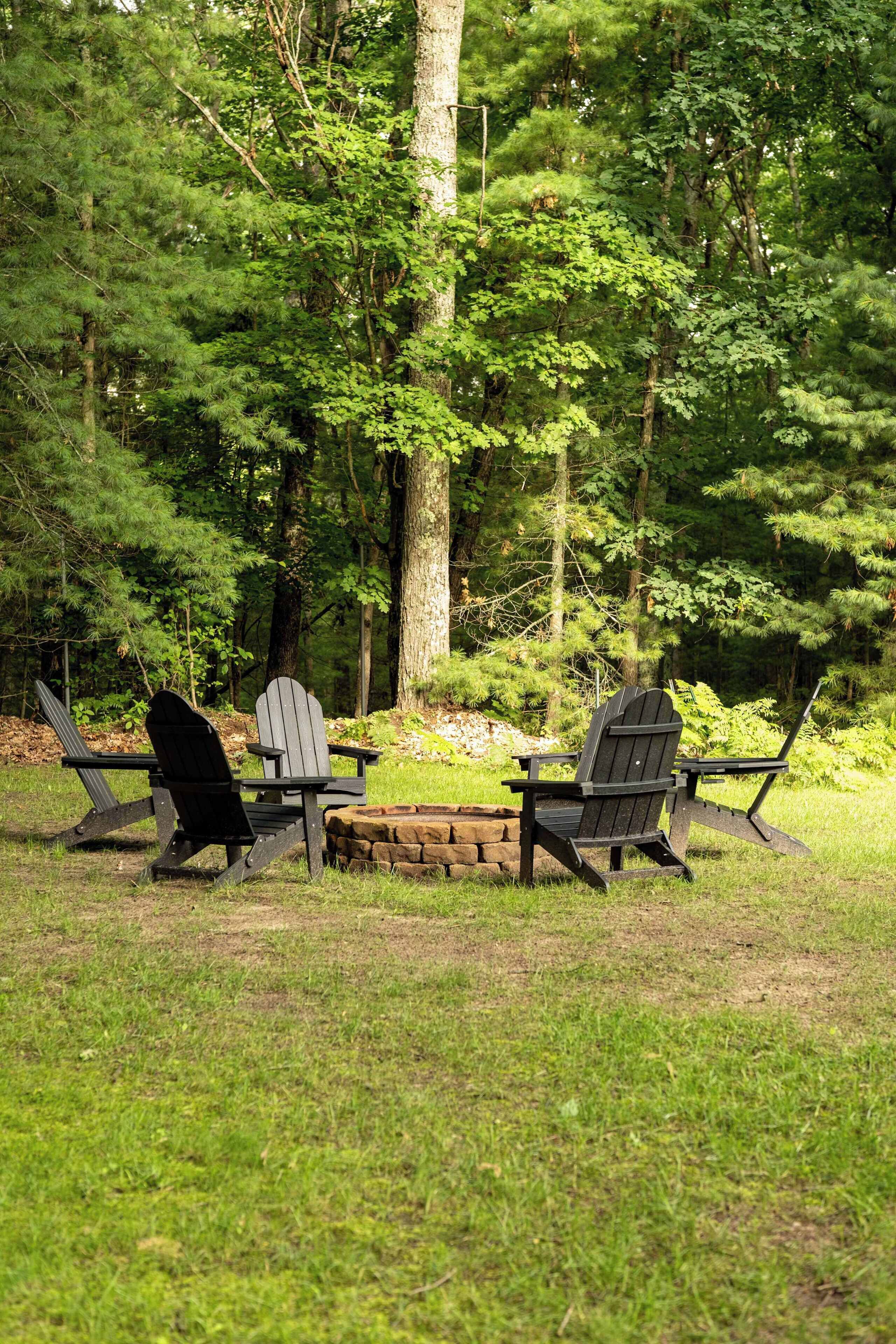 Ein Sitzbereich im Freien mit zwei Adirondack-Stühlen und einem kleinen Tisch, umgeben von bewaldeter Landschaft.