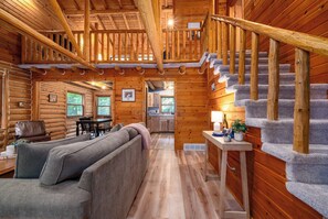 A log cabin interior with a living room, dining area, kitchen, and a staircase.