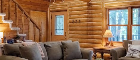 A log cabin interior with a wooden ceiling, a sofa, a coffee table, and a rug.