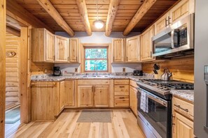 Cocina con armarios de madera, estufa de acero inoxidable y ventana con vistas a árboles.