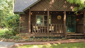 A wooden cabin with a porch, a welcome sign, and a green door.