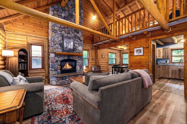 A log cabin interior with a stone fireplace, a sofa, a rug, and a dining area.