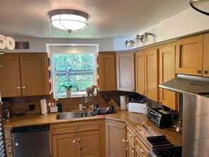 A kitchen with wooden cabinets, a built-in dishwasher, a window with a view of greenery, and a stainless steel range hood. - Pool - Roomy Historic Home on Beautiful Street Two Houses from the IntraCoastal (Lake Worth Beach)