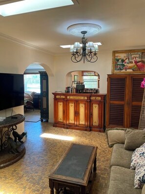 A living room with a television, a wooden cabinet, a sofa, and a chandelier. - Pool - Roomy Historic Home on Beautiful Street Two Houses from the IntraCoastal (Lake Worth Beach)