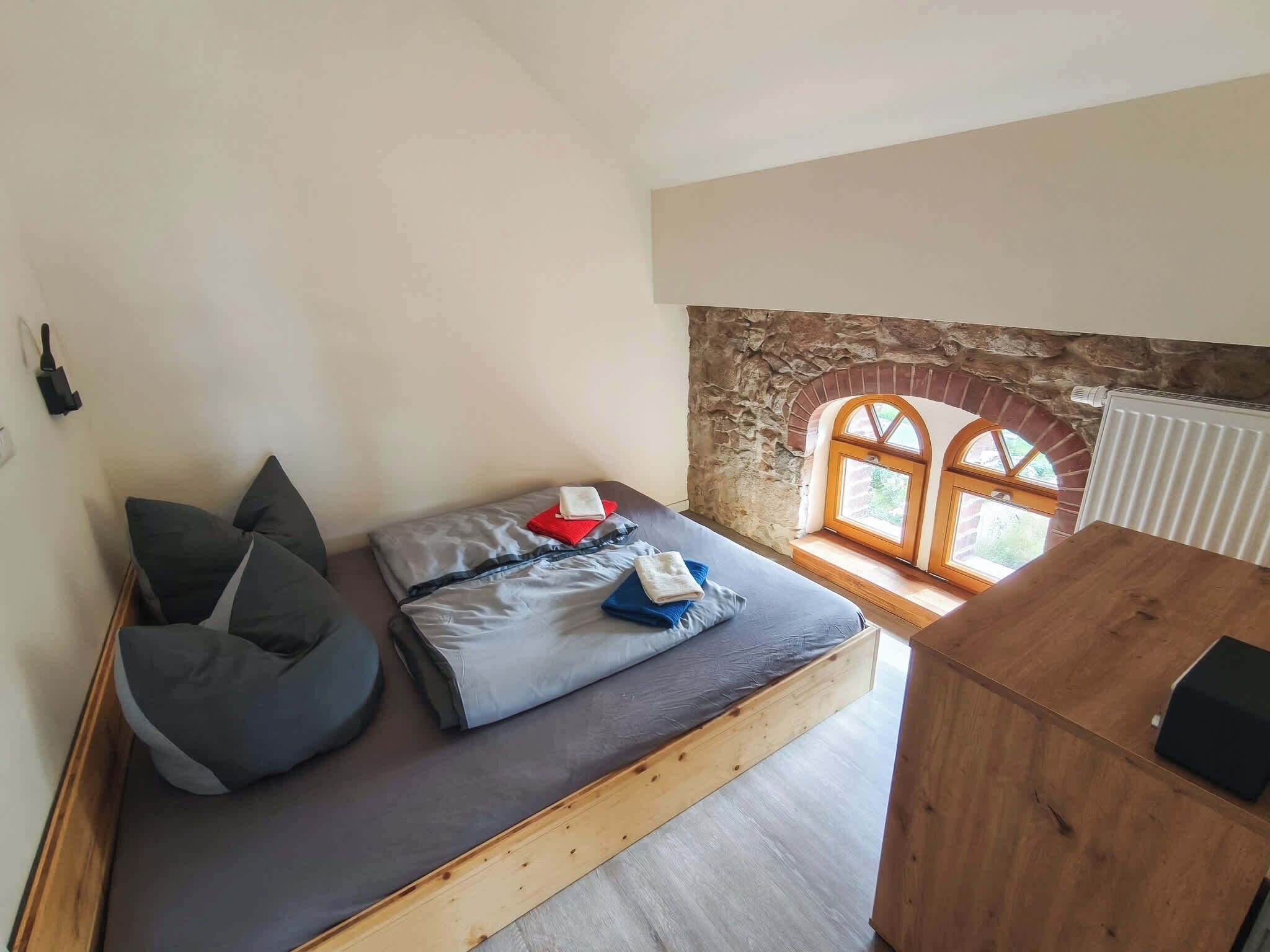 Een knus, klein kamertje met een bed, een bankje en een raam met een stenen boog.