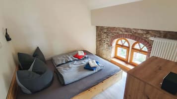 Een knus, klein kamertje met een bed, een bankje en een raam met een stenen boog.