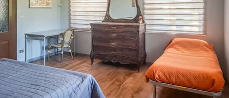A room with two beds, a dresser, a chair, and a window with blinds.