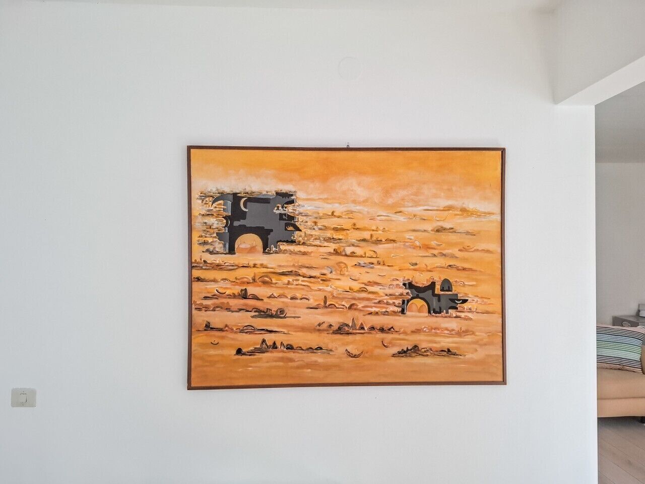 Dipinto di un paesaggio desertico con un cammello e un cavaliere, appeso a una parete in una stanza con un letto e un comodino.