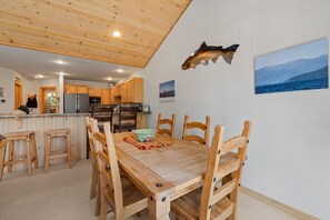 Ein Holzespeisesaal mit Stühlen, eine Küchenzeile mit Holzausstattung, eine Wanddekoration mit Fischen und ein gerahmtes Landschaftsbild.