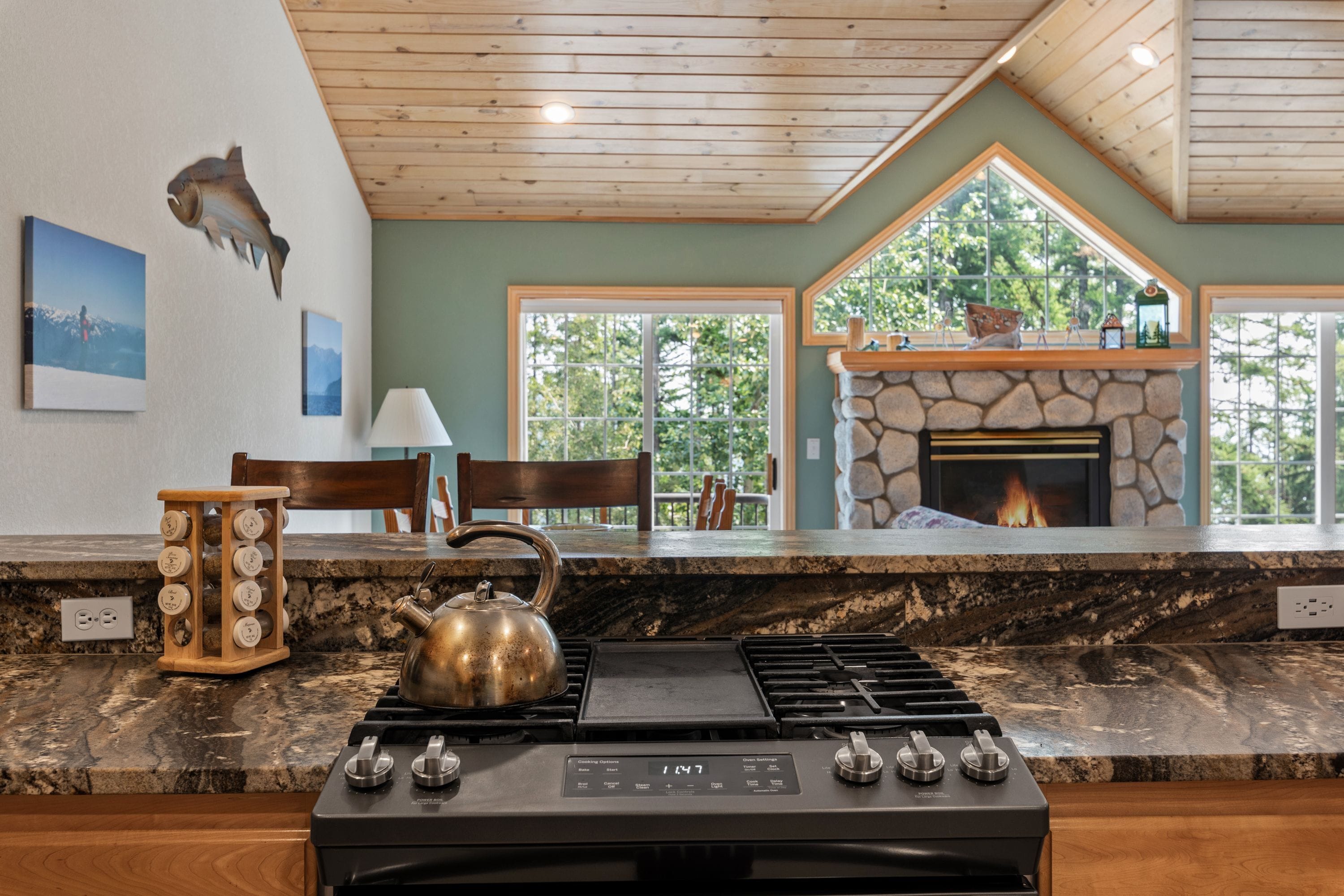 A kitchen with a gas stove, a kettle, and a stone fireplace.