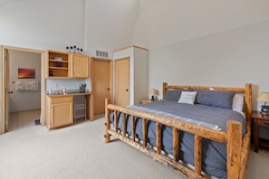 Ein Schlafzimmer mit einem hölzernen Bett, einer kleinen Küchenzeile und einem Badezimmer mit Handtuchhalter.