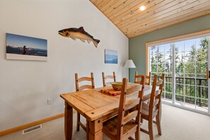 Een eetgedeelte met een houten tafel en stoelen, een visdecoratie aan de muur en een raam met uitzicht op bomen.