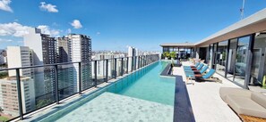 A rooftop infinity pool with a glass barrier, lounge chairs, and a city view. - COCDV0103 - Edificio Alive (Salvador)