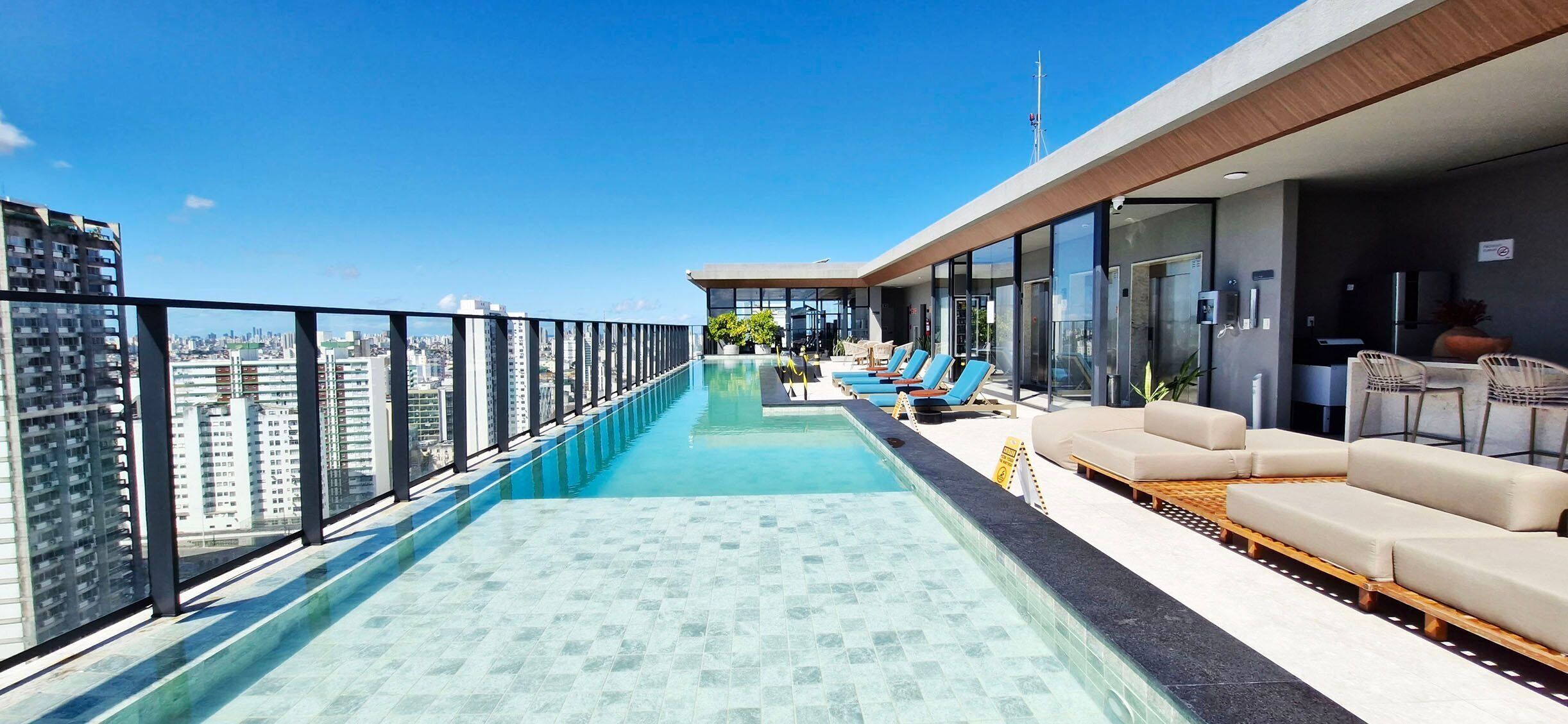 Ein Rooftop-Endlospool mit Stadtblick, Liegestühlen und einer modernen Außenküche.