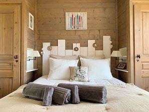 Ein Zimmer mit Holzwänden, einem Bett, Kissen, einem gerahmten Bild und einer Wandlampe.