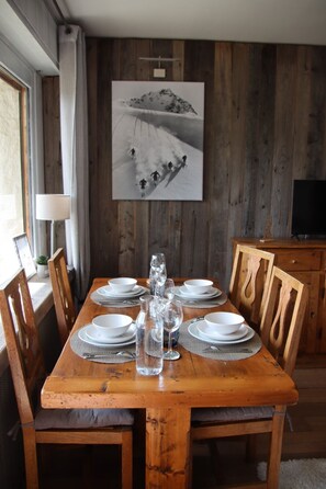 A dining table set with plates, glasses, and cutlery, surrounded by wooden chairs. - Charming 1-bedroom apartment in Megève, 10' walking of ski shuttle/village (Megève)