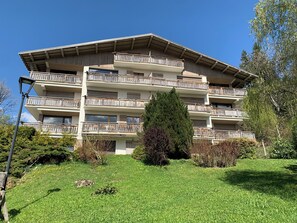 Ein mehrstöckiges Wohngebäude mit Balkonen, einer flachen Dachterrasse und einem gepflegten Rasen.