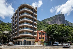 Ein mehrstöckiges Hotel mit geschwungener Fassade an einer Straßeneinmündung, mit Autos und einem Berg im Hintergrund.