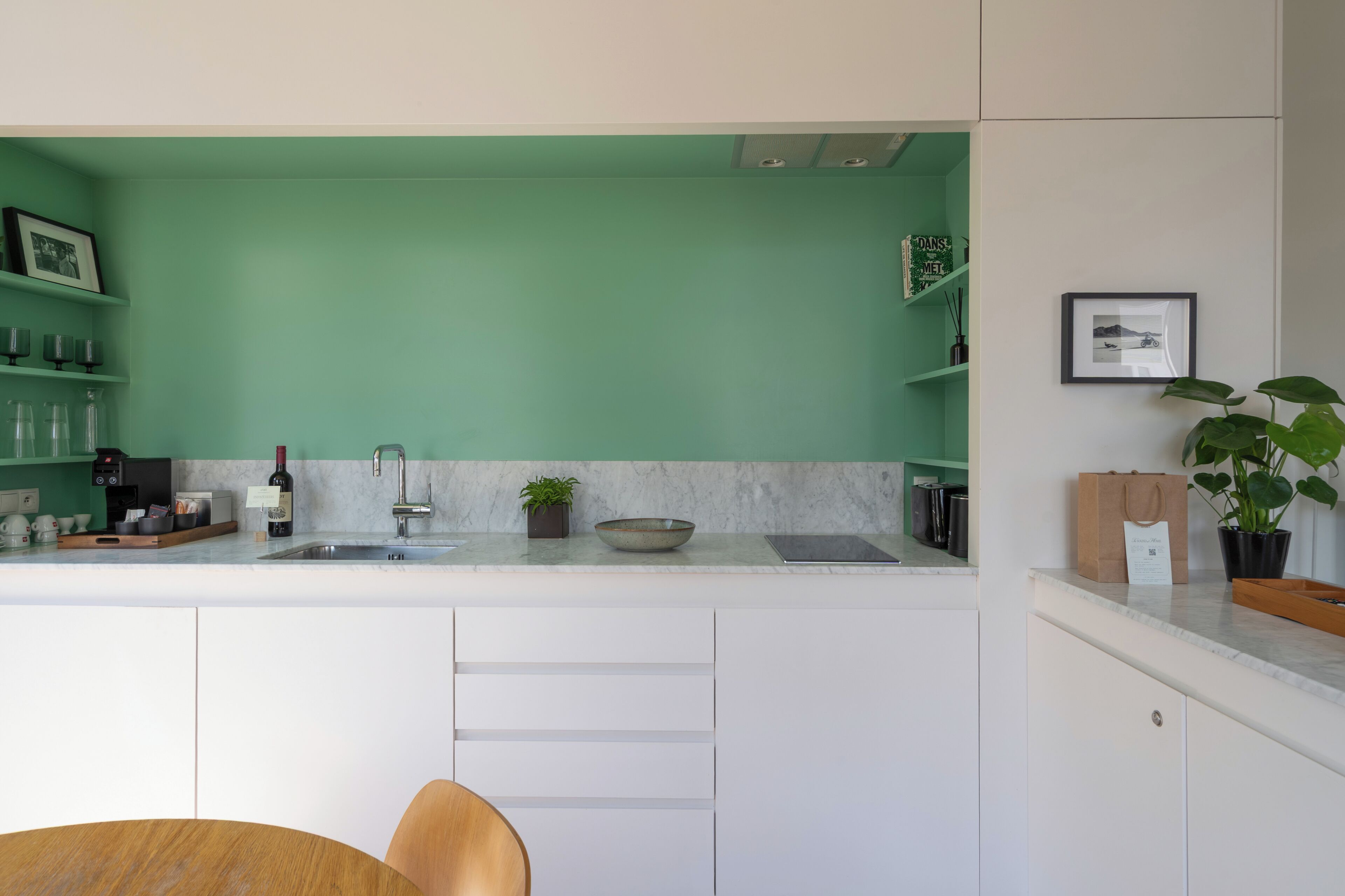 Een moderne keuken met een groene wand, witte kasten en een marmeren aanrecht.