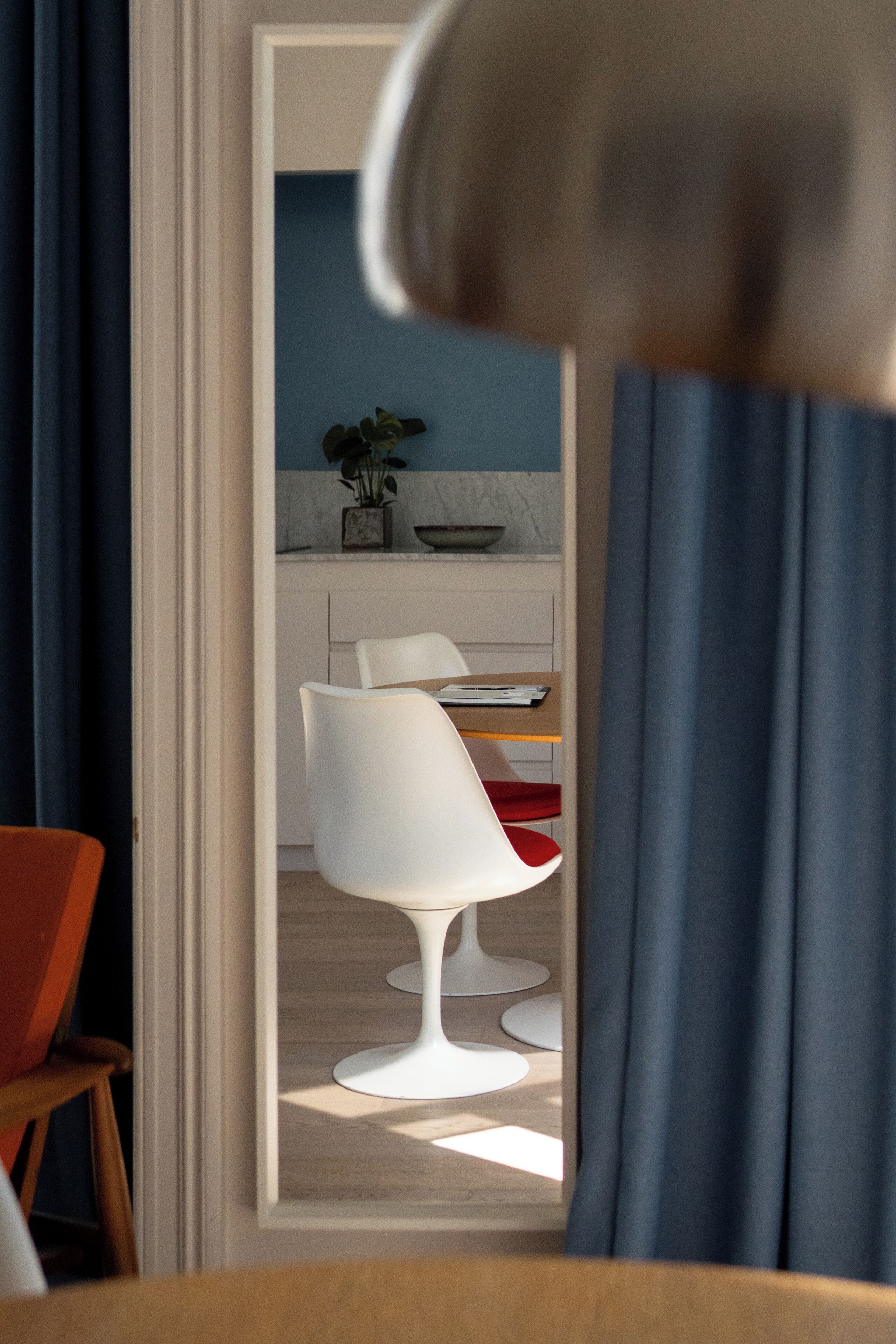 Een modern interieur met een eethoek met witte stoelen en een tafel, een keuken met een blauwe achterwand, en een potplant op het aanrecht.