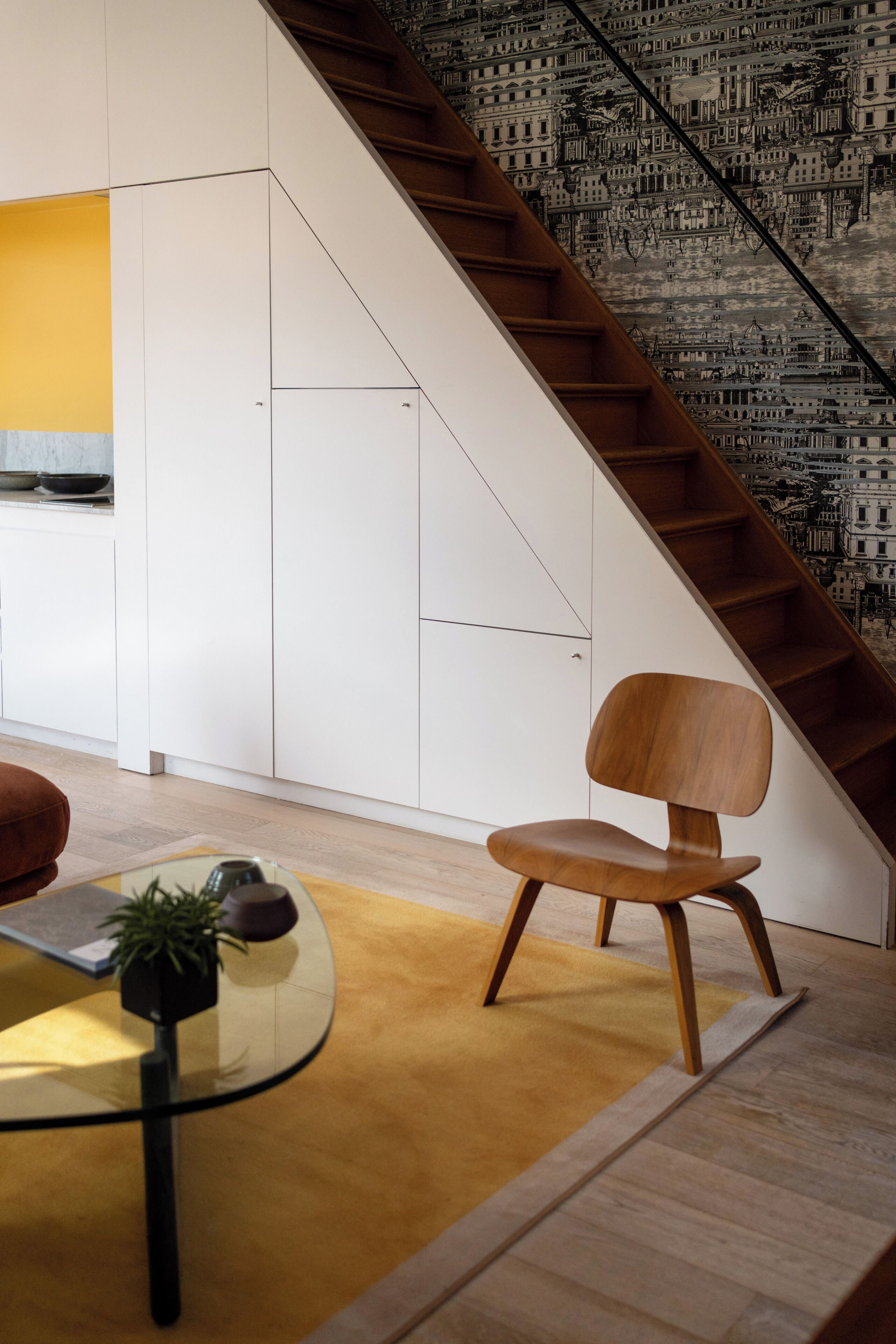 Un interior moderno con una escalera, una mesa de vidrio con una planta y una silla de madera.