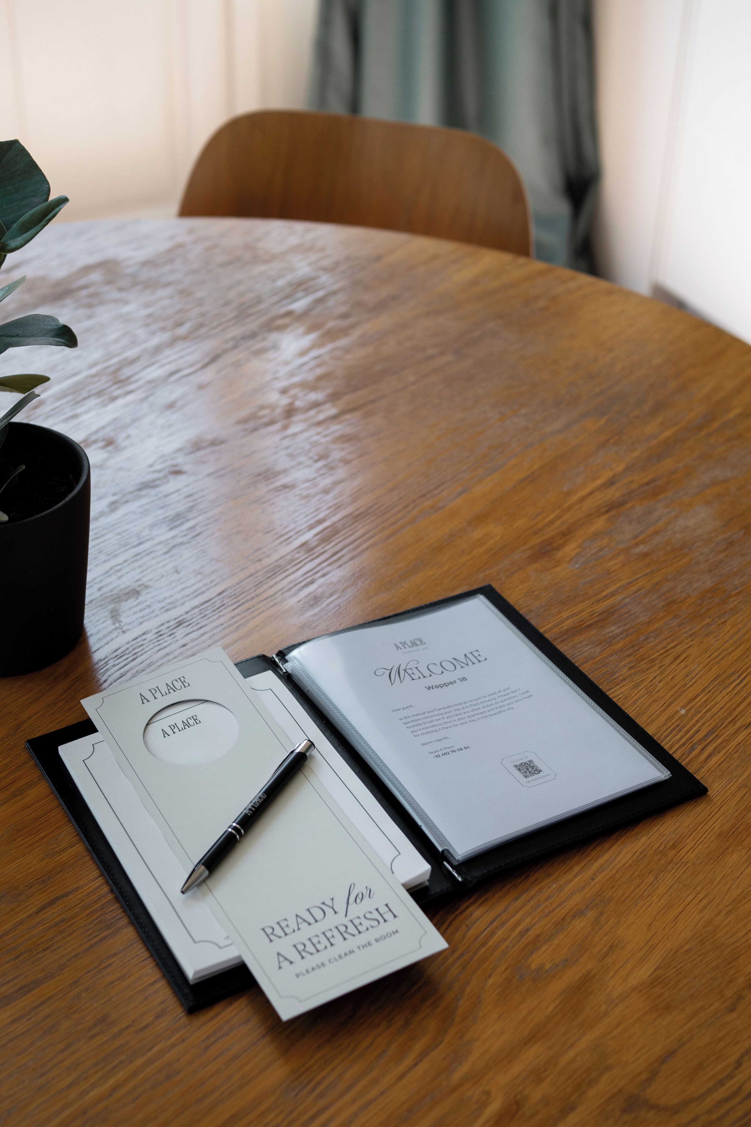 Une table en bois, avec un menu, un stylo et une plante en pot.