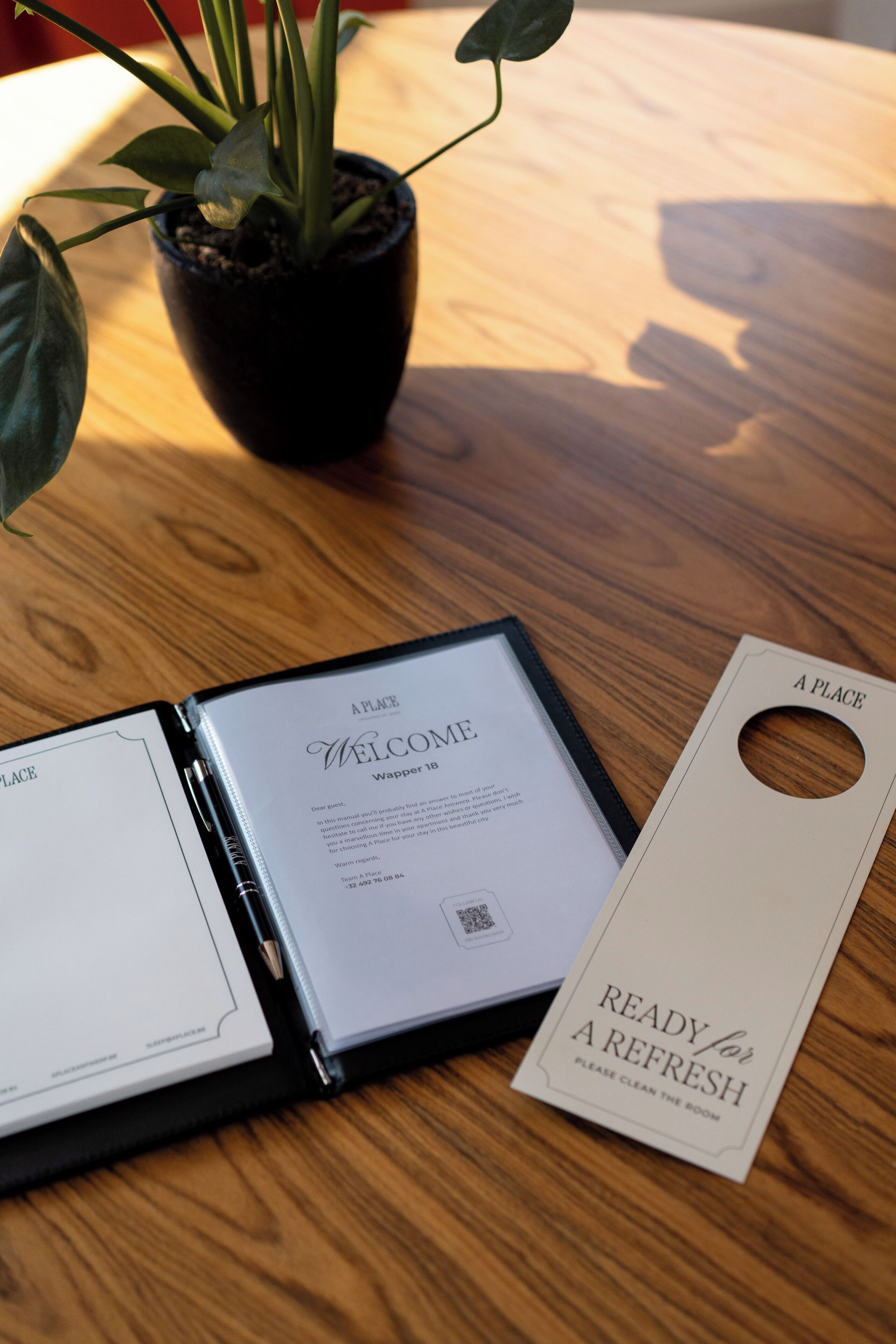 Een welkomstfolder, een sleutelkaart en een plant op een houten tafel.