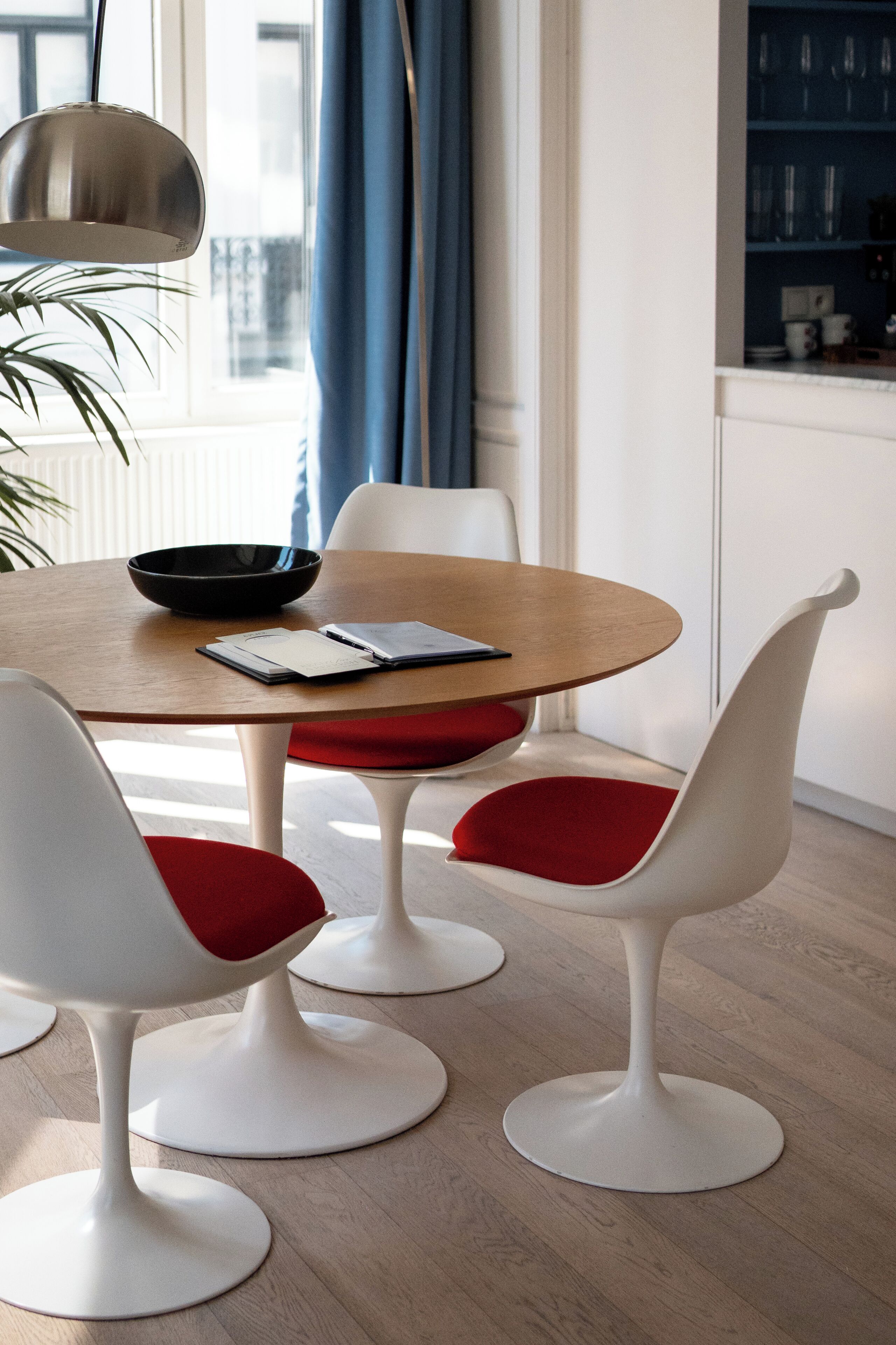 A modern dining area with a round table, white chairs with red cushions, a black bowl, and a book on the table.
