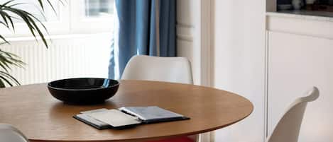 A modern dining area with a round table, white chairs with red cushions, a black bowl, and a book on the table.