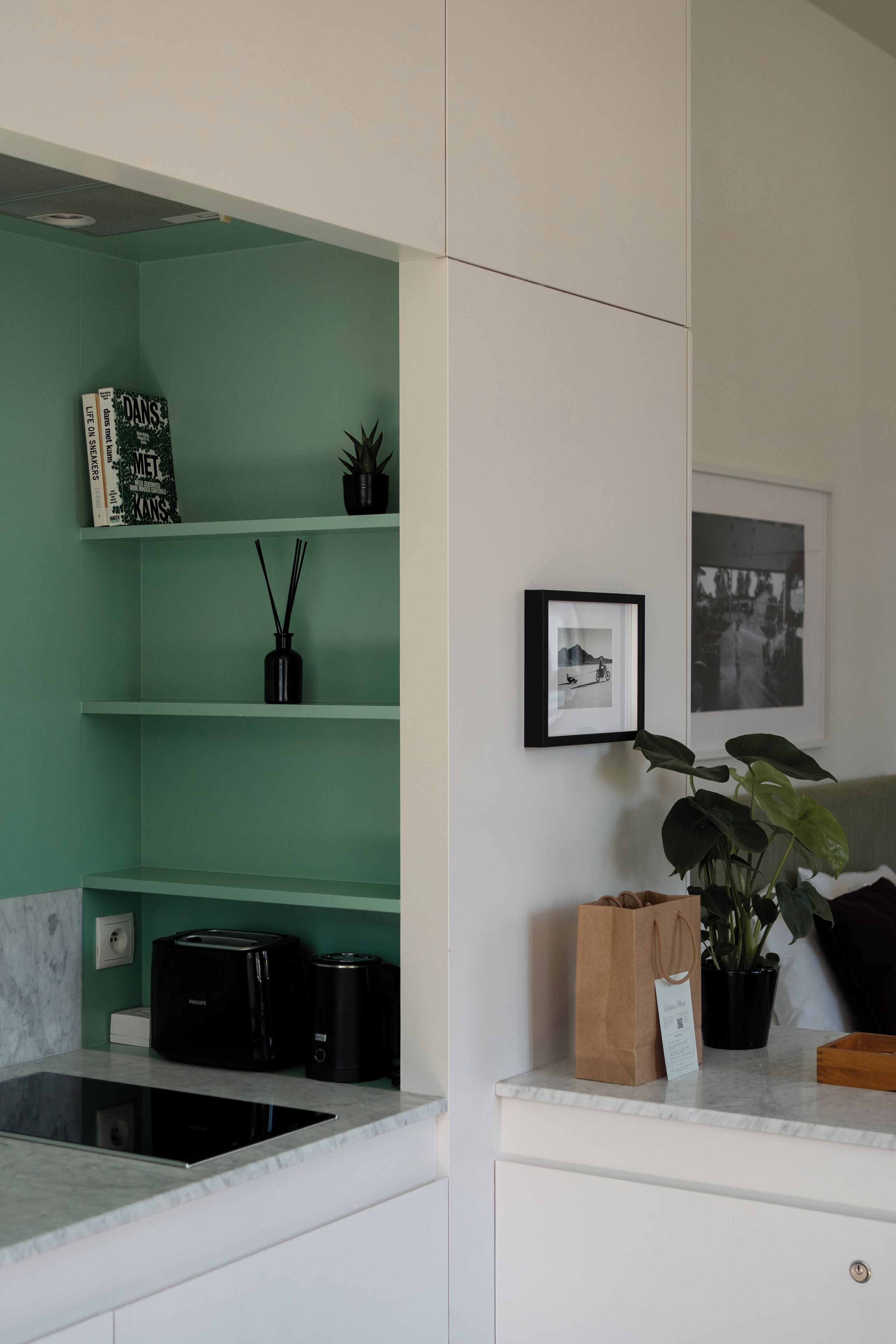 Una cocina con una pared verde, una cafetera, una planta y un cuadro en la pared.