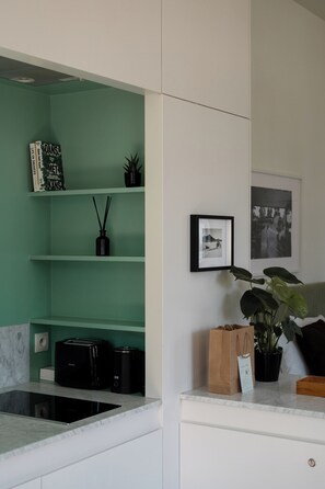 Uma cozinha com parede verde, máquina de café, planta e um quadro na parede.
