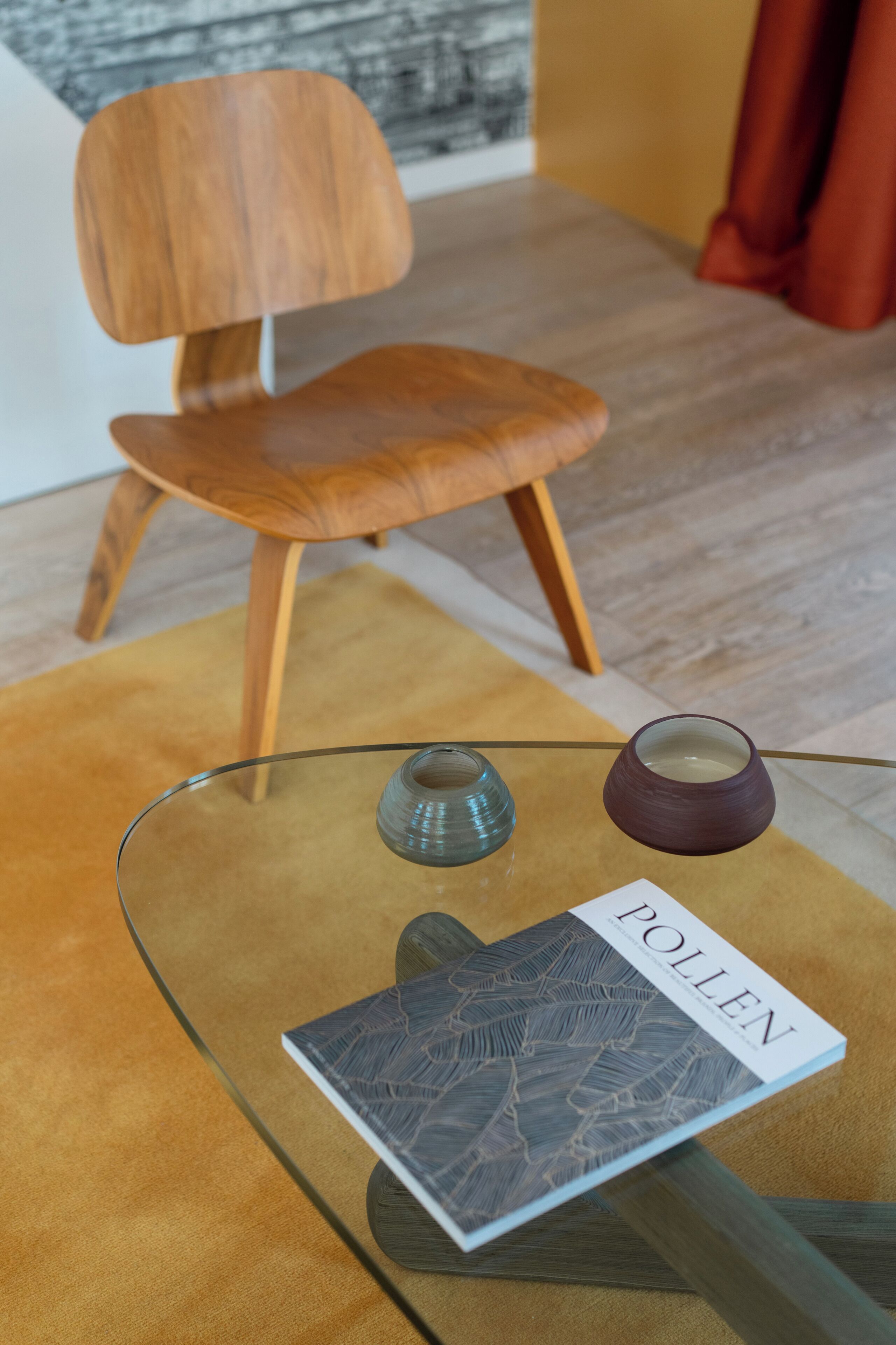 Een modern interieur met een glazen tafel waarop een boek met de titel 'POLLEN' ligt en een kleine vaas.