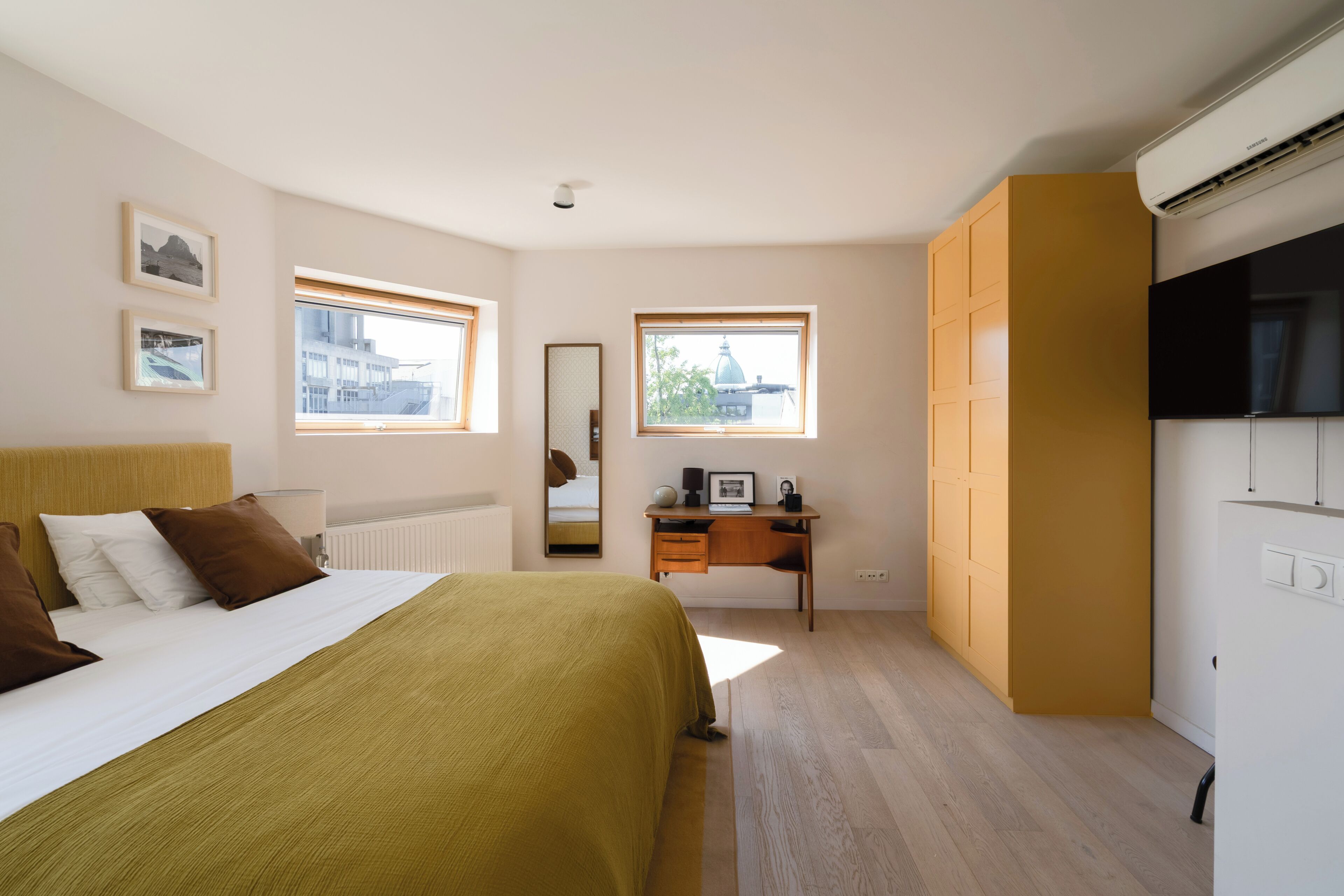 A bedroom with a bed, a desk, a mirror, and a wardrobe.