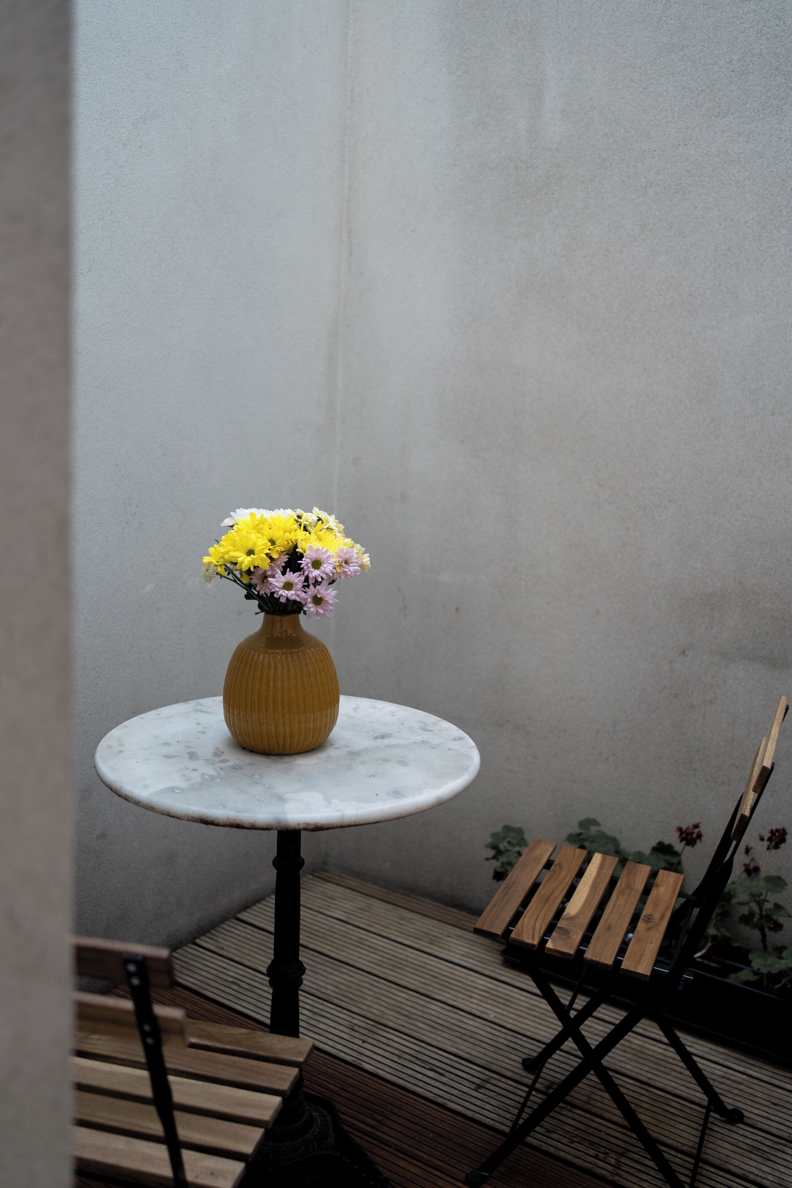 A small round table with a vase of flowers, a wooden bench, and a tiled floor.