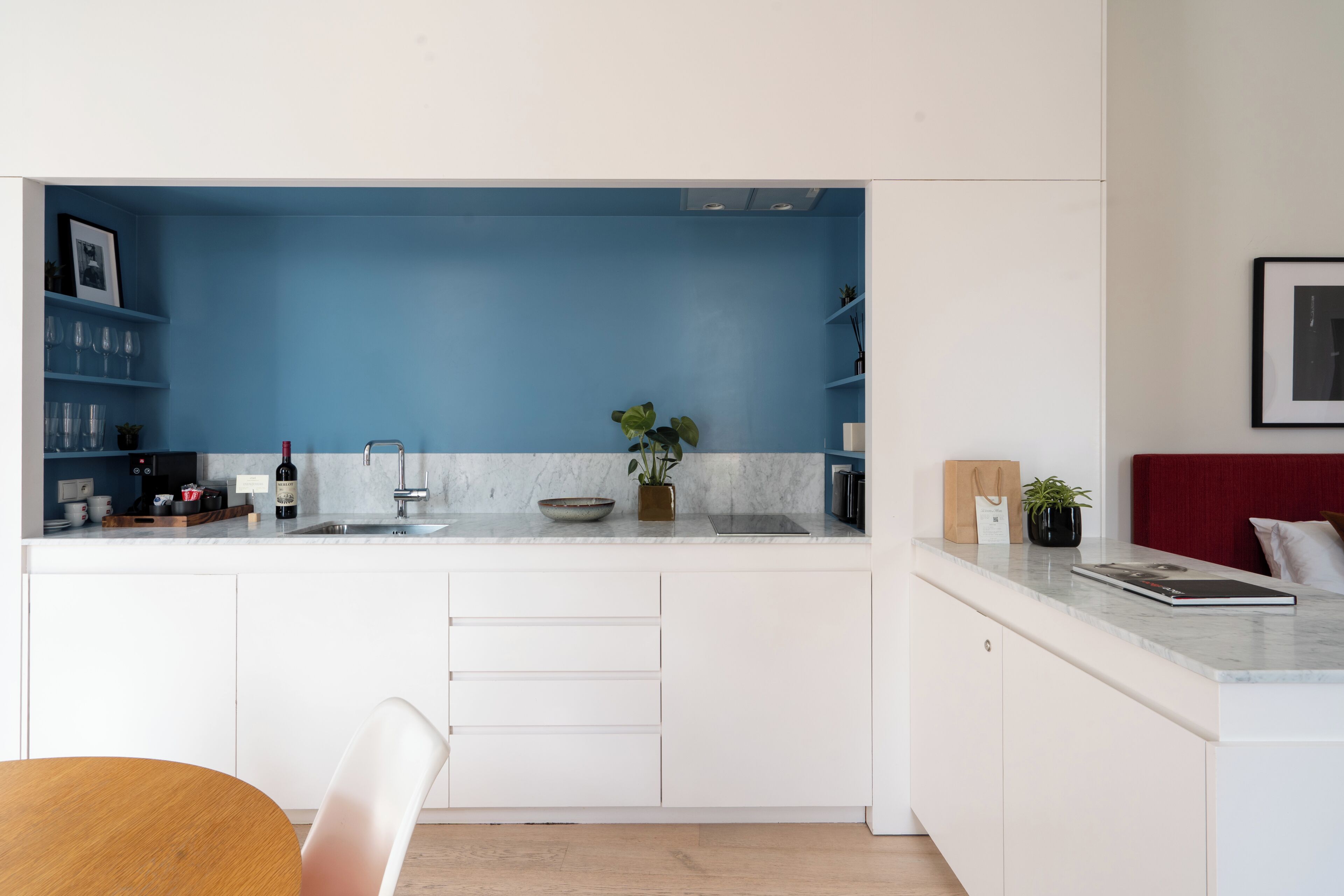 A modern kitchen with white cabinets, a blue accent wall, and a dining area with a wooden table and white chairs.