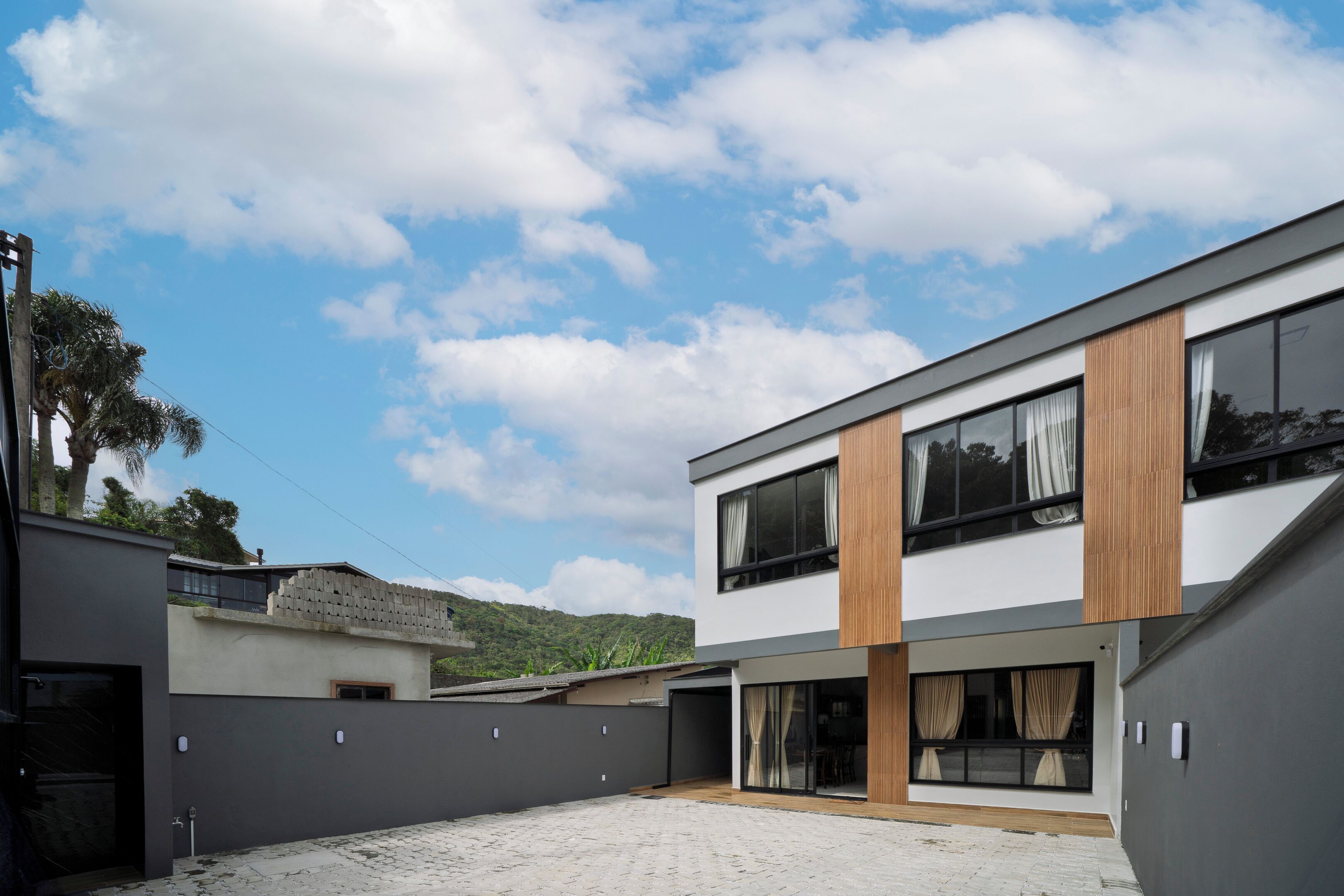 A modern two-story building with a flat roof, large windows, and a paved courtyard.