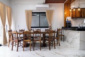 Un comedor con una mesa y sillas de madera, un equipo de aire acondicionado sobre la ventana, y una cocina con suelo de mármol y armarios de madera.