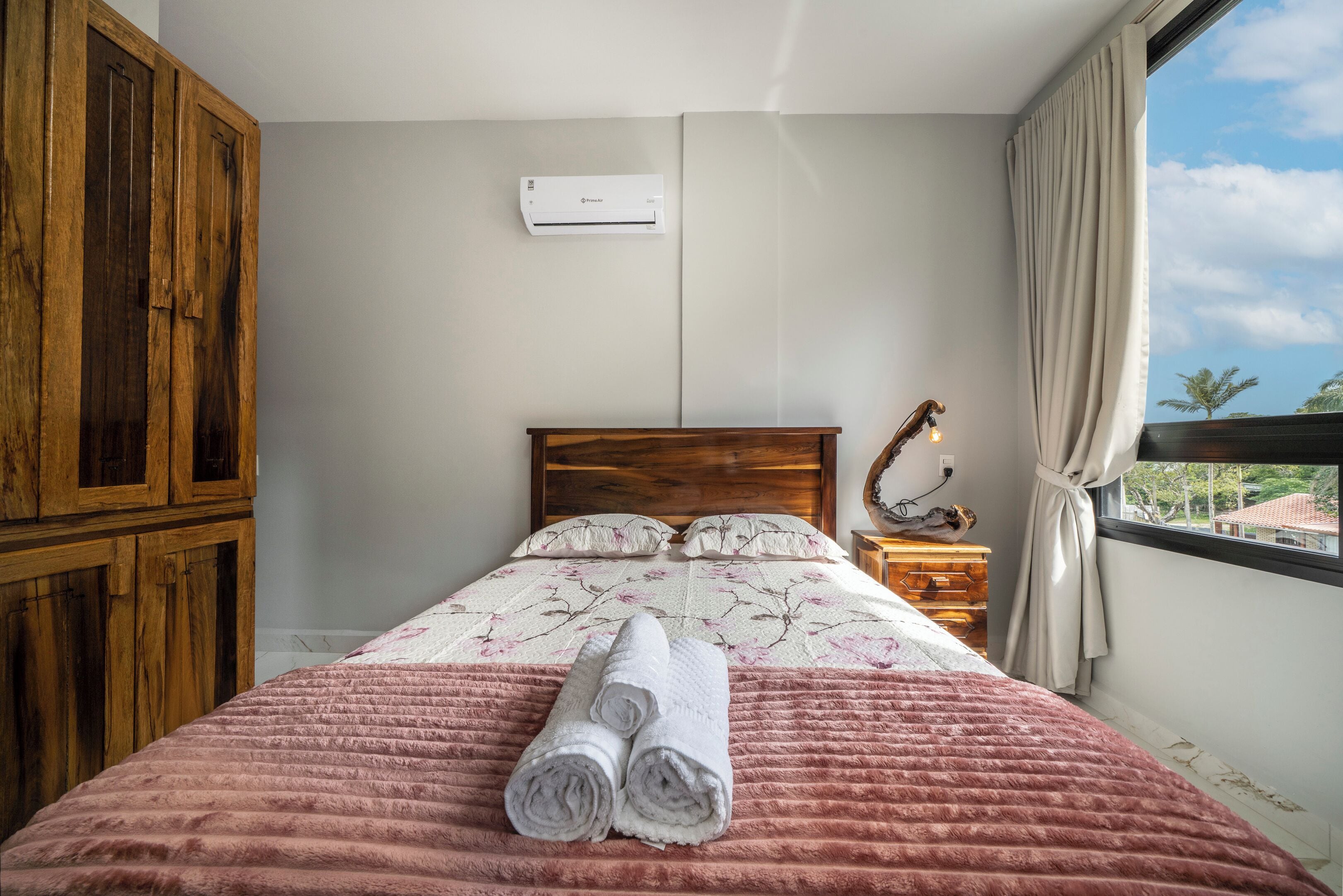 A bedroom with a bed, a wooden wardrobe, a bedside lamp, and a window with curtains.