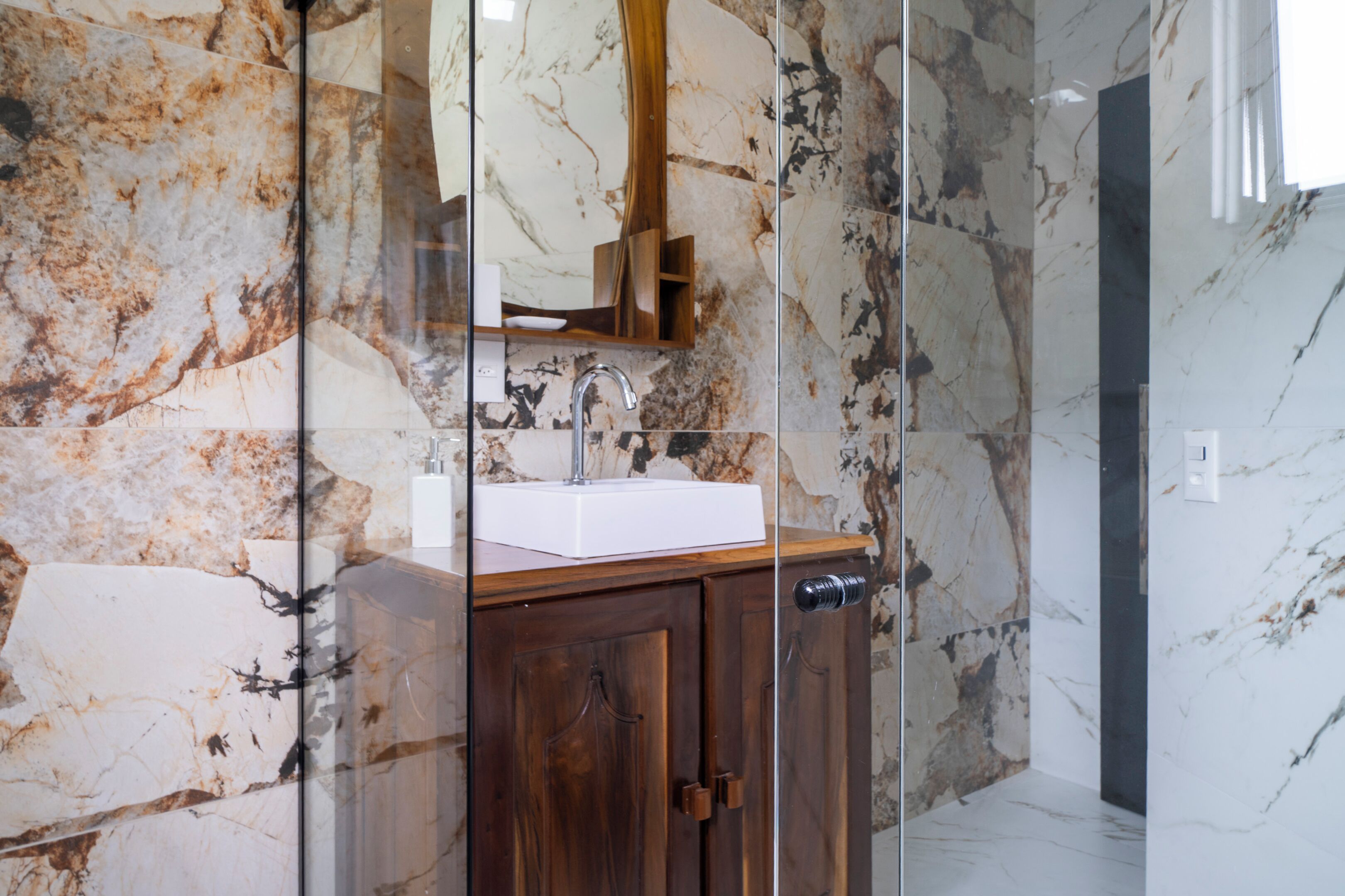 A bathroom with a marble wall, a wooden cabinet, and a white sink.