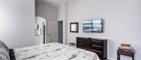 Un dormitorio con cama, cómoda, televisor y una mesita con libros.