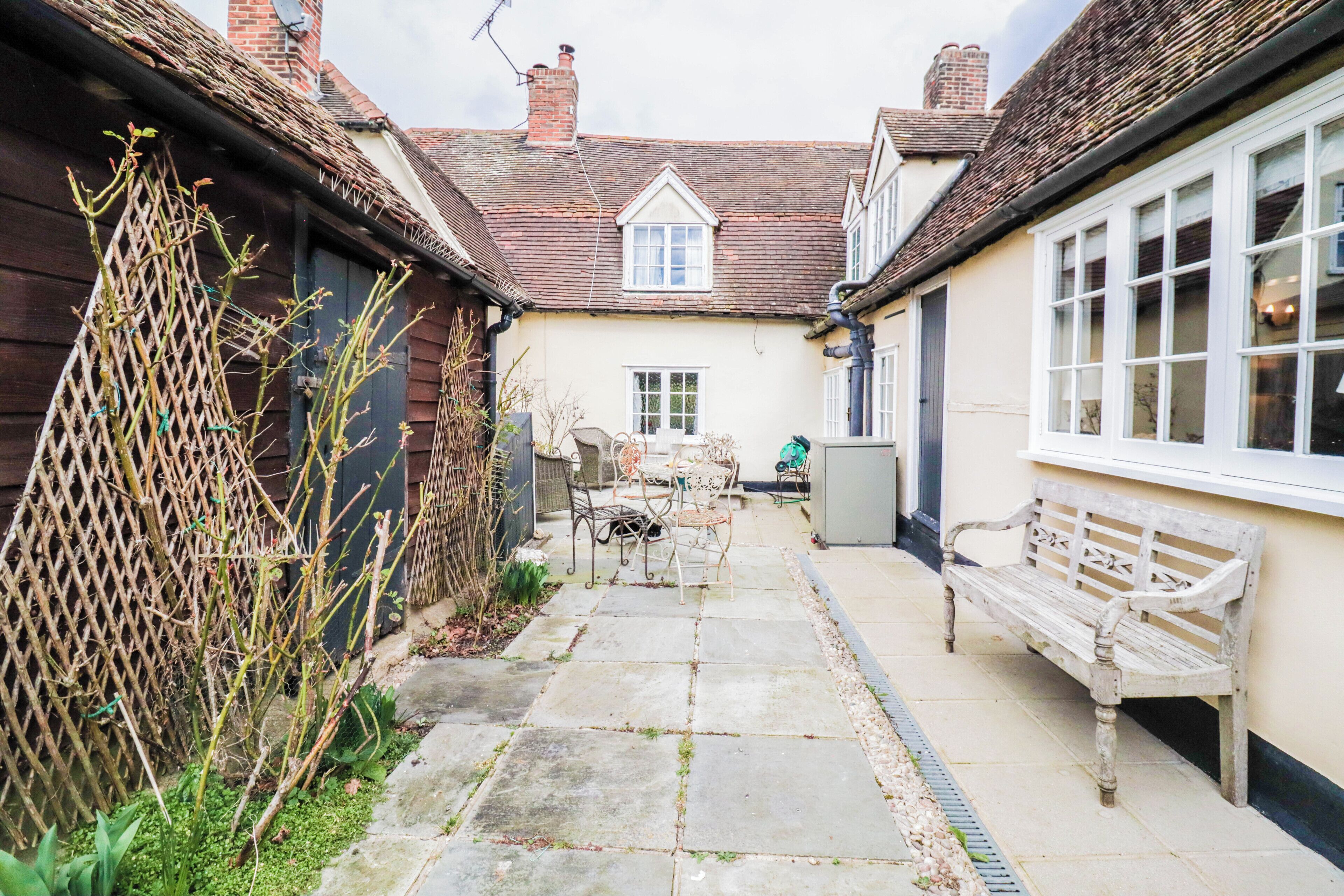 A narrow courtyard with a stone pathway, a wooden fence, and a bench.