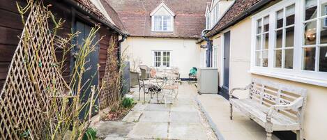 A narrow courtyard with a stone pathway, a wooden fence, and a bench.
