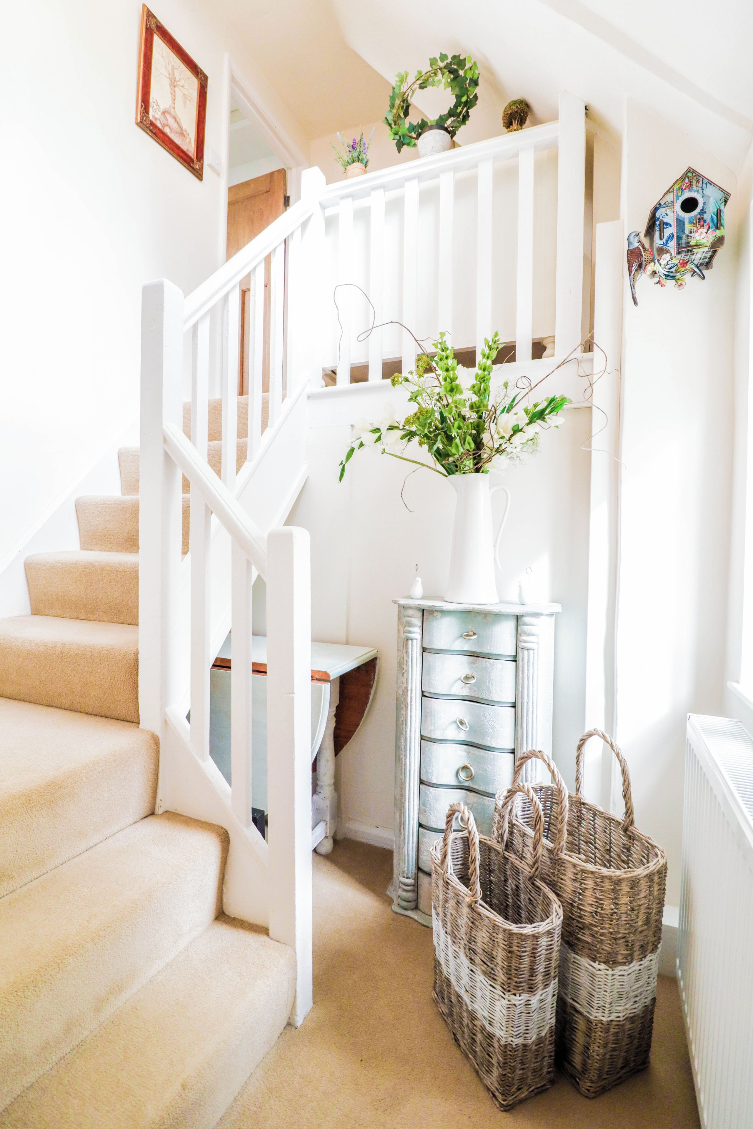 A staircase with a white railing, a white vase with flowers, and two wicker baskets.