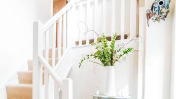 A staircase with a white railing, a white vase with flowers, and two wicker baskets.