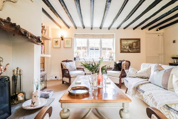 A cozy living room with a wooden coffee table, a fireplace, and a large window with white shutters.