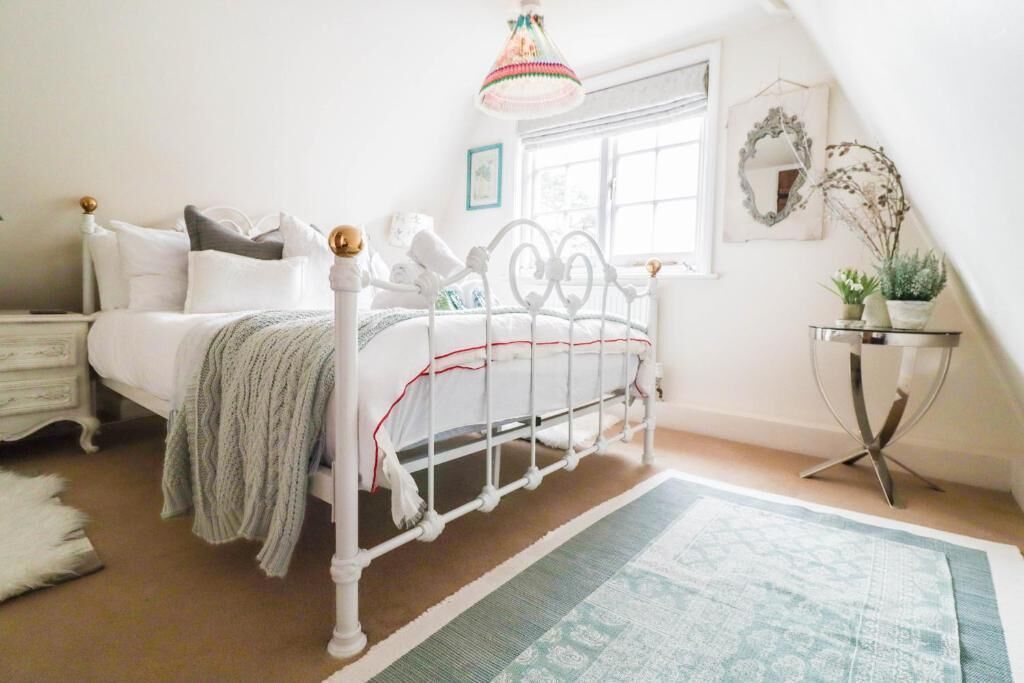 A bedroom with a white metal bed frame, a bedside table, a lamp, a window with a view, and a small table with a plant.