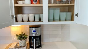 Eine Küchenschrank mit Kaffeemaschine, einem Dunkin' Kaffeebehälter und verschiedenen Tassen.