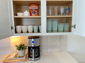 Eine Küchenschrank mit Kaffeemaschine, einem Dunkin' Kaffeebehälter und verschiedenen Tassen.