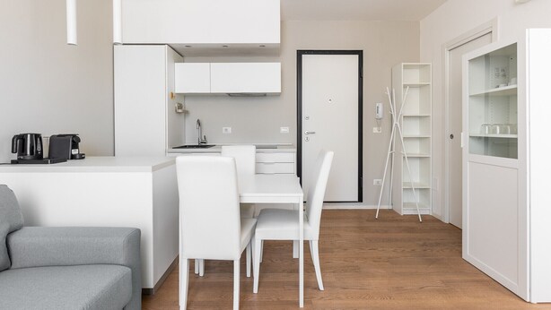 Une cuisine moderne avec des meubles blancs, une table à manger avec des chaises, une machine à café et un canapé blanc.