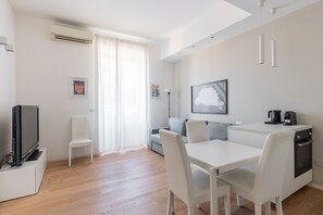 A modern living room with a flat-screen TV, a dining table with chairs, a sofa, and a coffee machine. - San Gervasio Apartment by Wonderful Italy (Bologna)